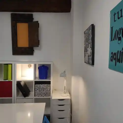Área de trabajo en 'Tu lugar de trabajo', con mesa blanca, estantería y decoración sencilla.