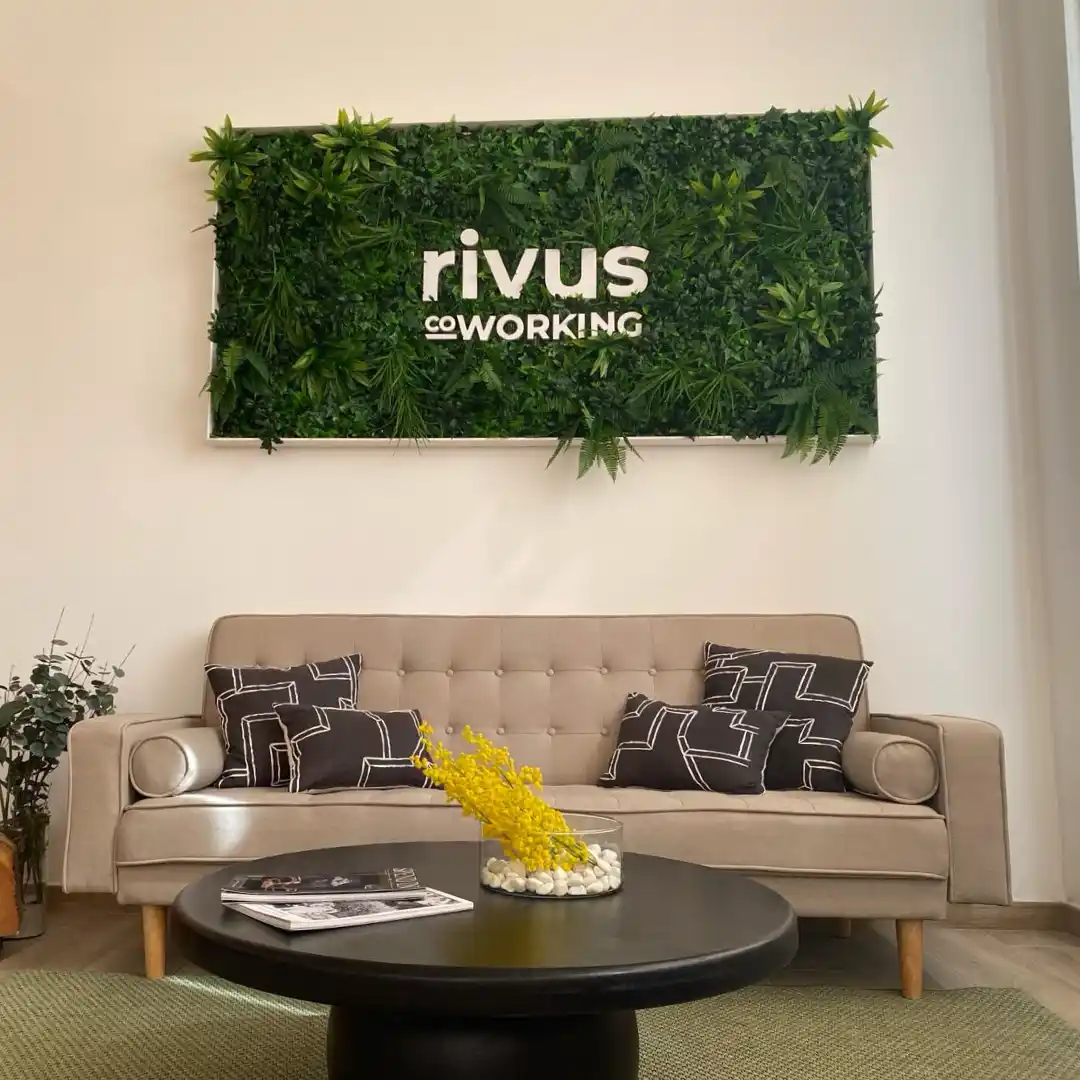 Área de descanso en el Coworking Rivus, con un sofá cómodo, mesa de centro y pared decorada con plantas.