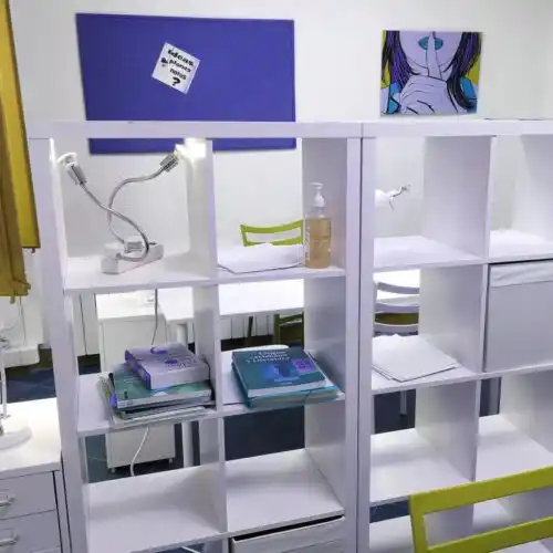 Estantería en 'Tu lugar de trabajo' con libros, lámparas y objetos decorativos coloridos