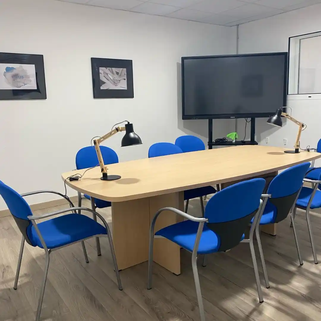 Sala de reuniones en el Coworking Rivus, con mesa grande, sillas azules y una pantalla para presentaciones.