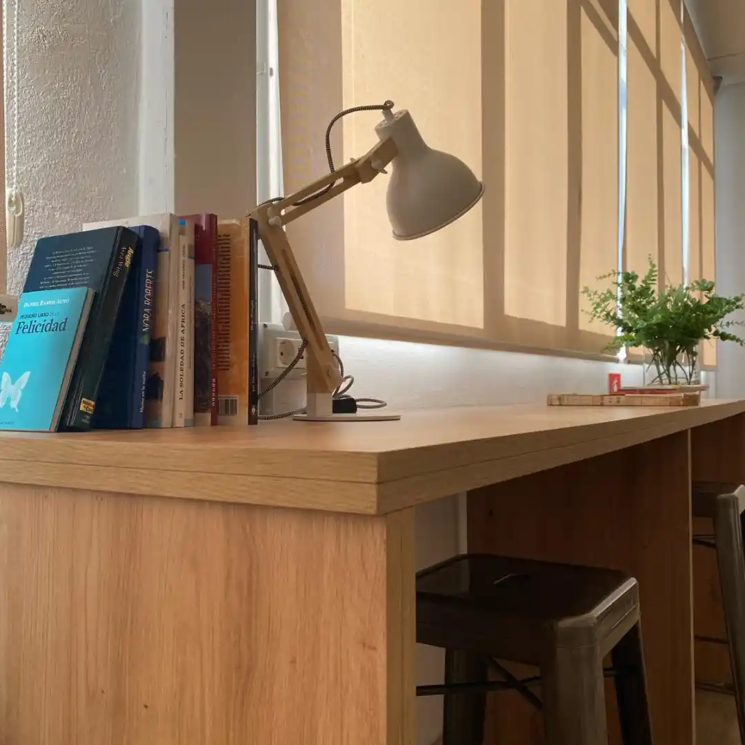 Espacio de trabajo en el Coworking Rivus, con mesa de madera, lámpara de escritorio y libros decorativos.