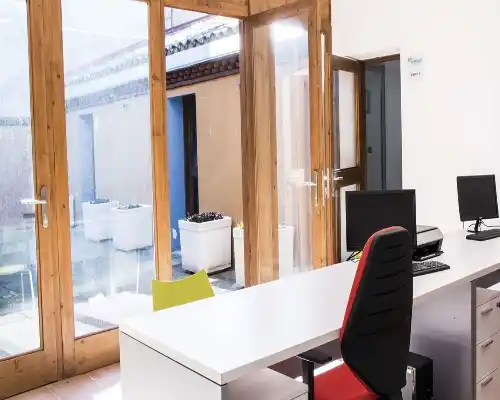 Vista desde otro ángulo de la oficina en el Centro Pedrola, mostrando una puerta doble de vidrio abierta que da al patio.