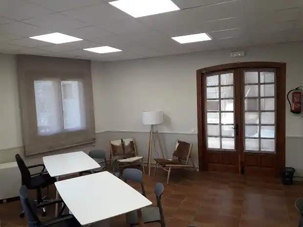 Sala de coworking en el centro de Boltaña con mesas blancas y sillas modernas.
