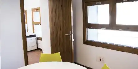 Interior de oficina en el Centro Pedrola con puerta y ventana de madera, mesa redonda y silla verde.