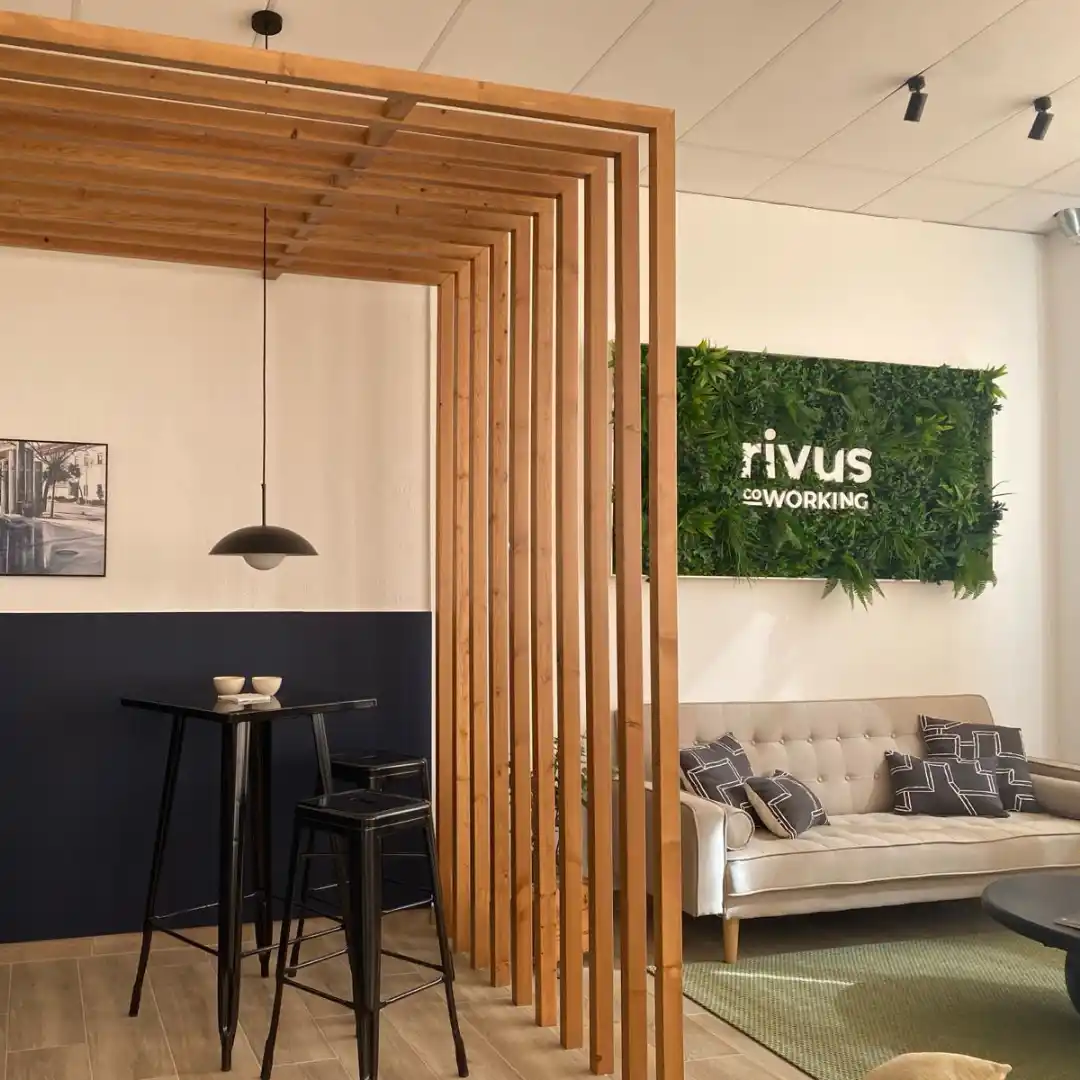 Zona de descanso en el Coworking Rivus, destacando una estructura de madera con plantas decorativas y un sofá