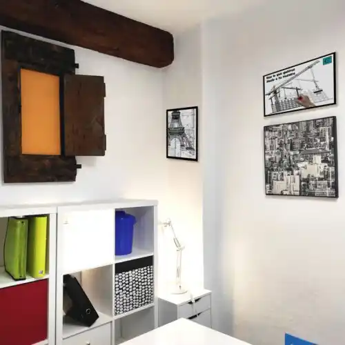 Oficina colorida en 'Tu lugar de trabajo', con estanterías, decoración de cuadros y muebles funcionales.