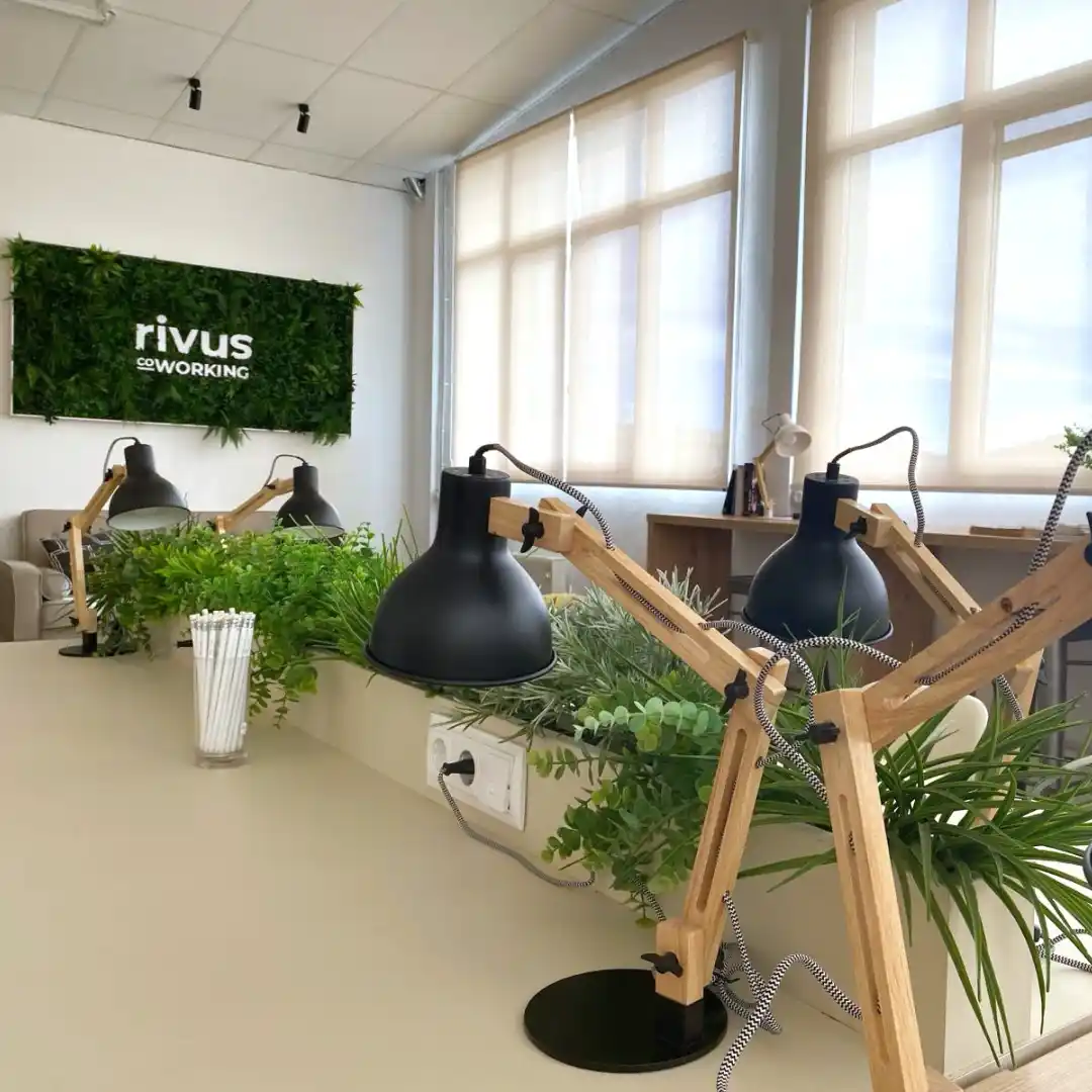 Mesa de trabajo en el Coworking Rivus, con lámparas de escritorio de madera y plantas decorativas.