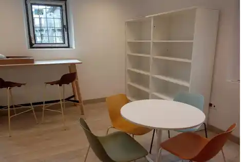 Área común con sillas coloridas y estanterías en Broto.