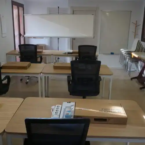 Espacio de trabajo con escritorios, sillas y una pizarra.