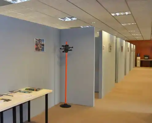 Oficinas separadas con paneles grises, mesas y una percha naranja.