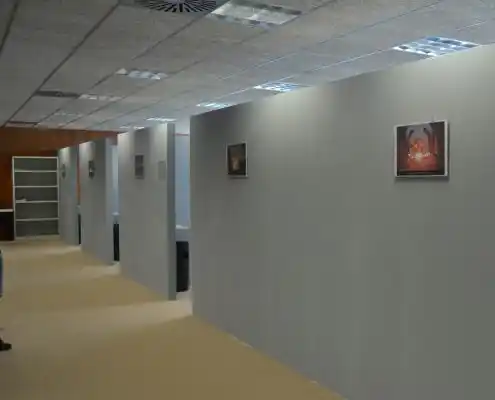 Pasillo con oficinas separadas por paneles y cuadros en las paredes.