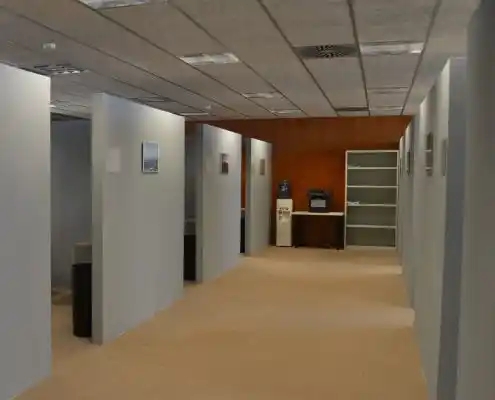 Oficina compartida con paneles grises, estantería y agua embotellada.