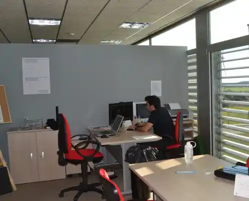 Oficina con mesa de trabajo y una silla roja, más estantería con papeles.