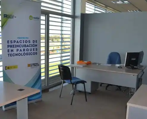 Oficina vacía con un escritorio blanco y una silla azul, acompañado de una pared blanca.