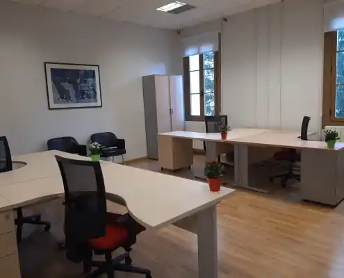 Espacio de oficina en el Centro Sabiñánigo, con escritorios, sillas rojas y grandes ventanales.