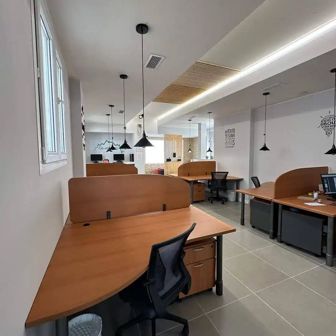 Oficina en el Centro Pirineos con escritorios y boxes de madera, sillas, y lámparas negras colgando del techo.