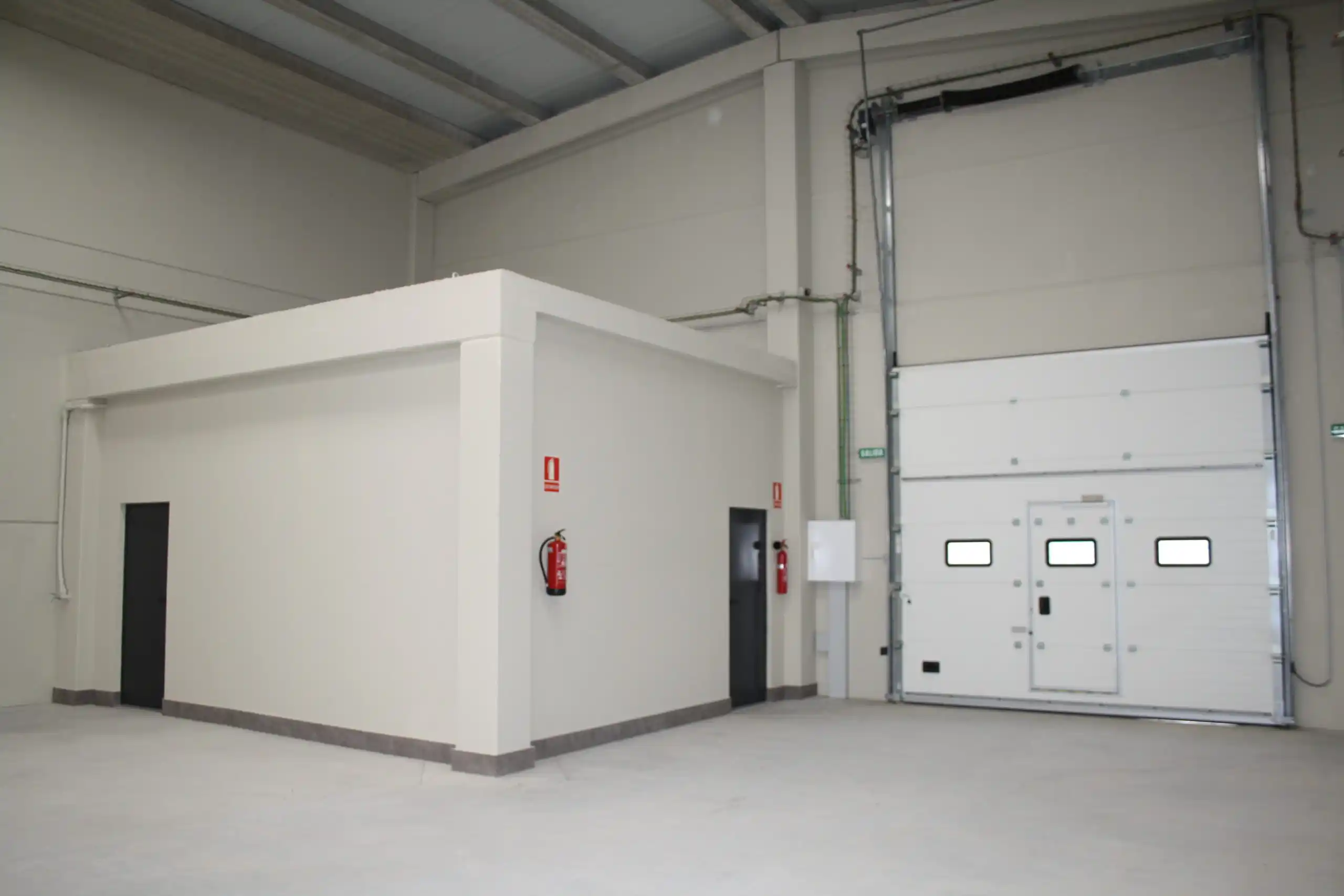 Espacio industrial vacío con garaje y extintores.