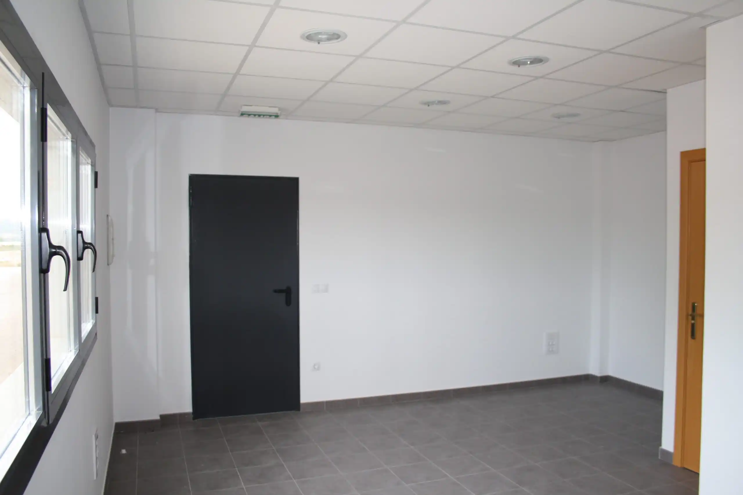 Oficina vacía con paredes blancas y puerta negra.