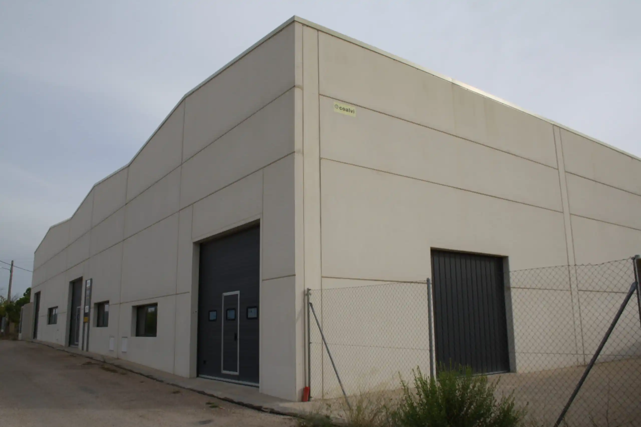 Fachada exterior de un edificio industrial con puertas y cercado.