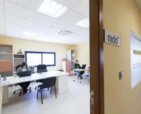 Oficina con señalización 'nido' y dos personas trabajando en sus escritorios.