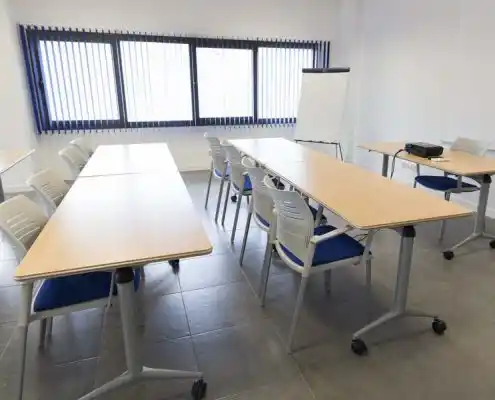 Sala de reuniones en el centro Mequinenza equipada con mesas y proyector.