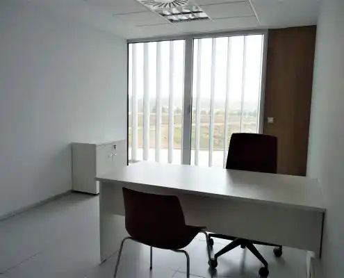 Oficina en el centro con un amplio ventanal, mesa blanca moderna y sillas negras.