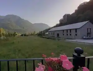 Vista de un campo verde con árboles, flores y montañas al fondo. En el centro, un edificio de coworking se encuentra entre el paisaje natural.