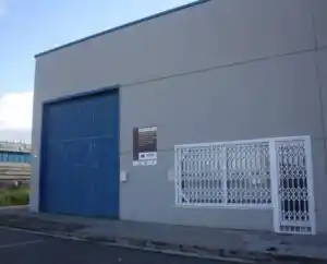 Vista exterior del edificio en Jaca, de color gris, con una puerta azul de gran tamaño y ventanas con rejas blancas.