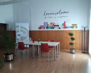 Espacio de trabajo en el Centro Sabiñánigo, con mesa blanca, sillas rojas y mural inspirador.