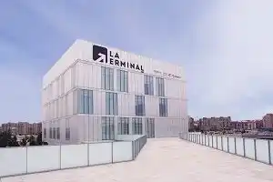 Vista exterior del Centro Zaragoza La Terminal, un edificio grande y blanco con numerosas ventanas y su logo visible en la parte superior.