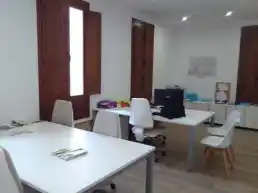 Oficina del Centro Mas de las Matas con mesas de trabajo, sillas y ventanas grandes.