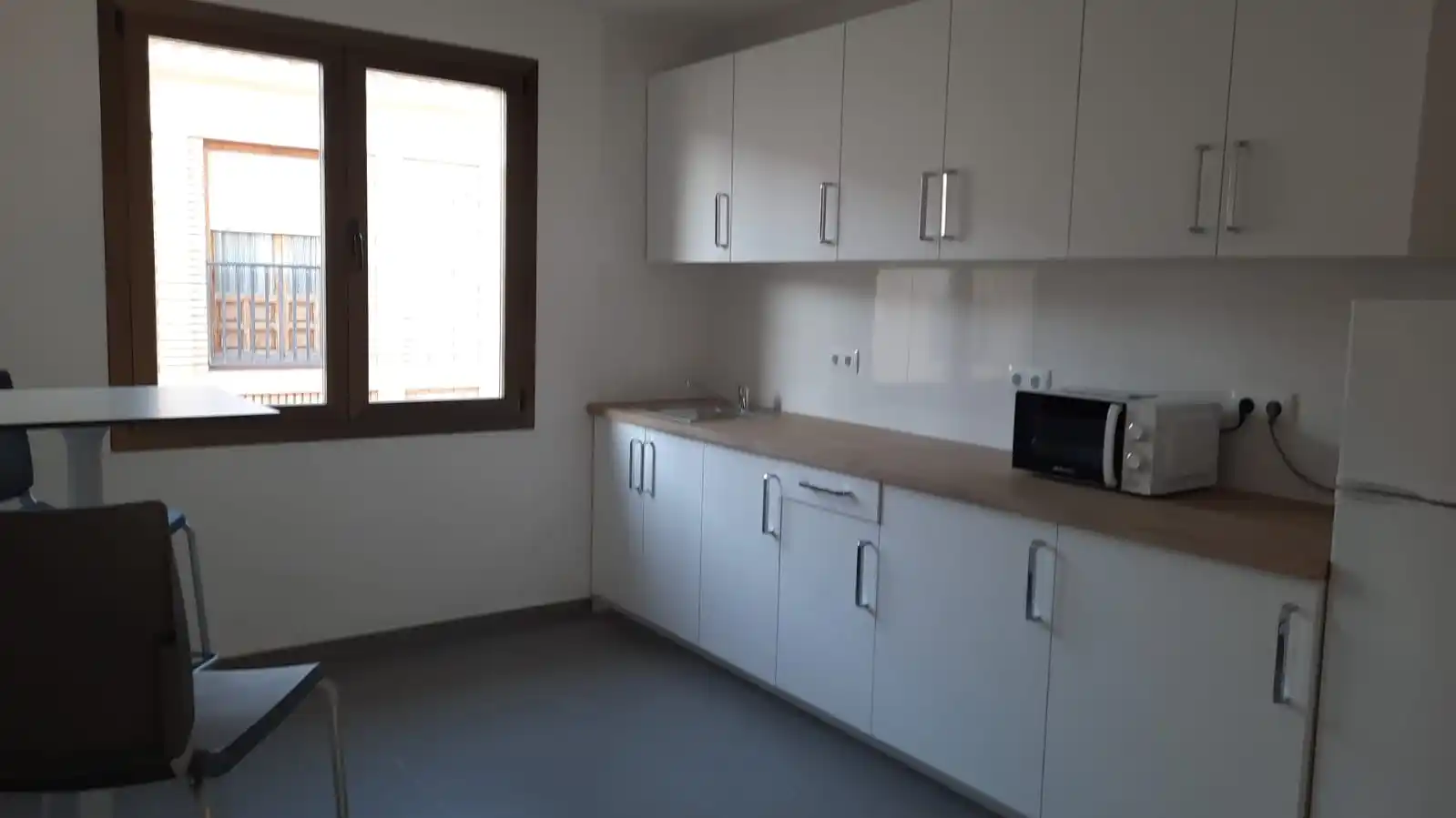 Ventana con marco de madera, mesa larga y alacena con varias puertas blancas.