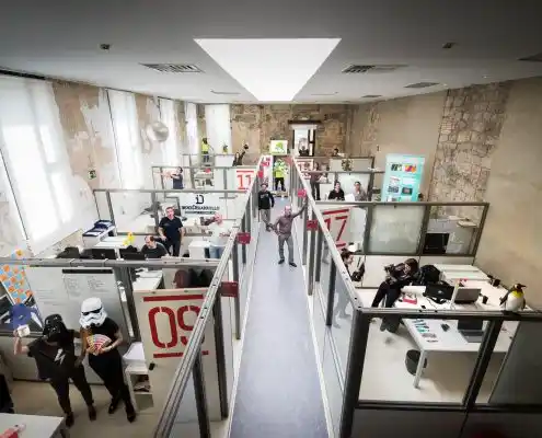 Espacio de trabajo compartido en el Centro Zaragoza Activa, con cubículos de trabajo transparentes y personas colaborando.