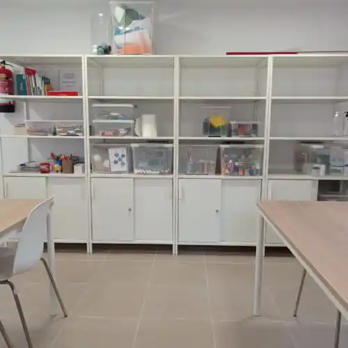 Estanterías blancas organizadas con material de oficina en el coworking de Moyuela